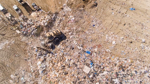 A large dumpster is seen in the middle of a pile of trash. The trash is scattered all over the ground, and the dumpster is surrounded by a lot of debris. The scene is chaotic and messy