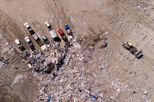 A pile of trash and a few trucks are in the background. The trucks are parked in a line, and the pile of trash is in the foreground. Scene is one of waste and pollution, with the trucks