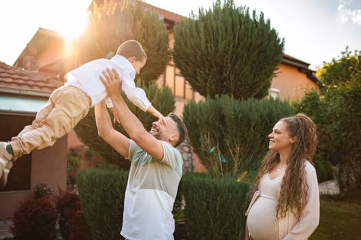 Father lifts son happily while expecting mother smiles nearby