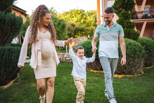 Expecting parents smile while walking with their child outdoors.