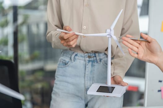 A business professional holds a wind turbine model, discussing sustainable energy solutions and ESG principles in a corporate setting.