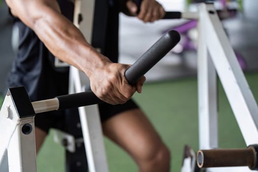 A young man grips gym equipment tightly, emphasizing strength and focus during his fitness training session.