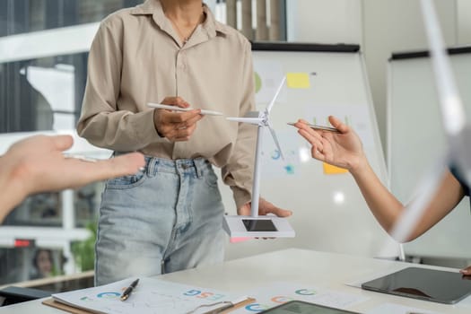 A team brainstorming about sustainable initiatives, using wind turbine models to visualize their ESG goals in a modern workspace.