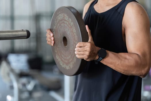 A young man engages in strength training by lifting a weight plate, showcasing dedication to fitness and physical health.