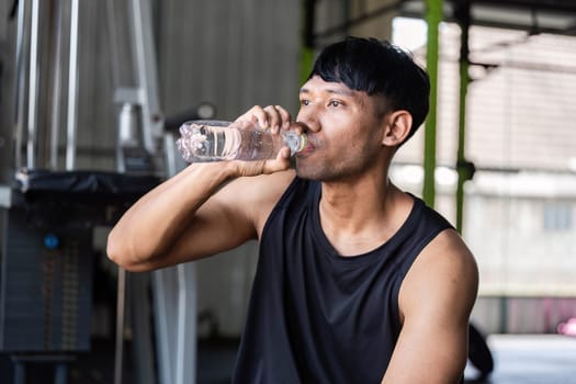 A man takes a refreshing drink of water while resting at the gym, emphasizing the importance of hydration in fitness.