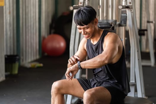 A joyful man at the gym checks his fitness watch, celebrating progress and enjoying his fitness journey.