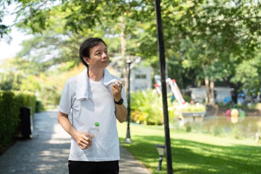A man pauses on his morning walk to hydrate with a bottle of water, promoting wellness and healthy living in a serene park setting.