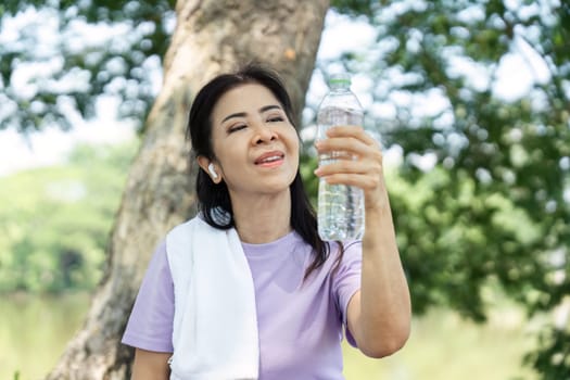A joyful woman holds a water bottle, enjoying the refreshing taste of hydration after a workout in a peaceful park.