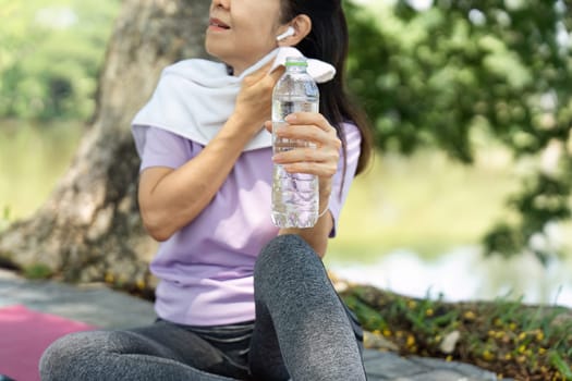 A woman takes a moment to hydrate with water after a workout session in a serene outdoor setting, promoting wellness and fitness.