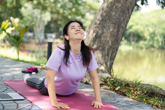 A woman practices yoga on a pink mat in a tranquil outdoor space, promoting wellness and mindfulness.