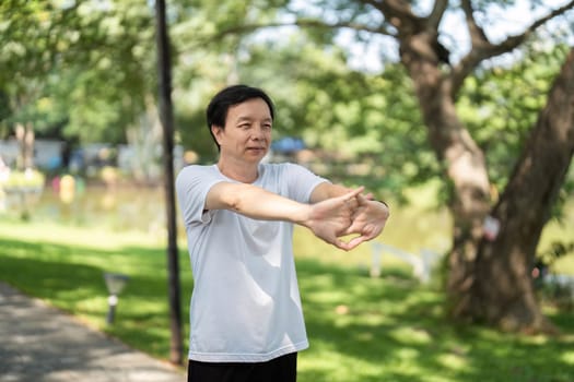 An elderly man stretches his arms outdoors, focusing on mindfulness and relaxation in a serene park atmosphere.