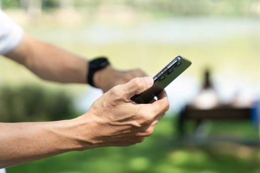 An elderly man checks his smartphone outdoors, integrating technology into his wellness routine in a peaceful park environment.