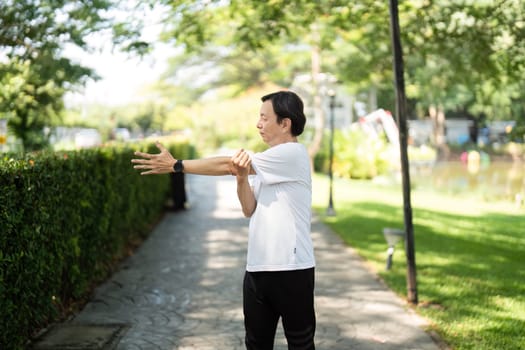 An older man practices arm stretches outdoors, emphasizing flexibility and wellness in a tranquil park setting.