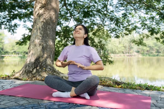 A woman sits cross-legged on a yoga mat, practicing mindfulness and meditation in a tranquil lakeside setting.