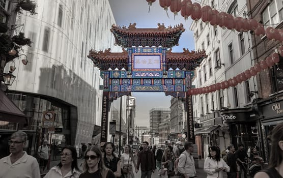 London, UK - May 13, 2025 - Crowd of people visit London Chinatown entrance gate in traditional chinese design with glazed yellow tiles, a golden dragon, painted panels, two white jade plaques and red lanterns, The Chinese text translates "Peace and Prosperity (Zhong guo tai ping) to Chinatown". use it as your Wallpaper, Poster and Copy space, Selective focus.
