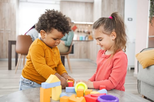 Two young children play with colorful building blocks at home.