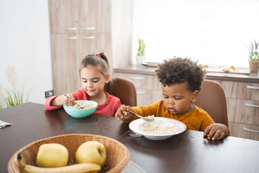 Two kids are happily eating breakfast at the kitchen table.