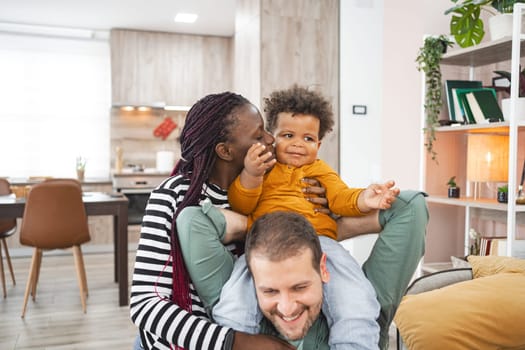 A mother and father playfully interact with their young child indoors.