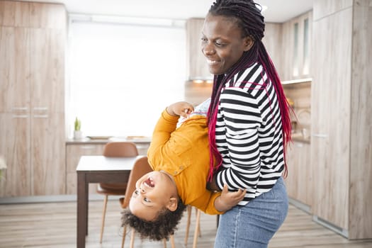 A mother joyfully plays with her child in a modern kitchen.