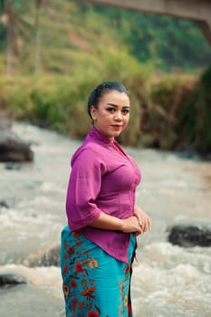 Asian woman standing in front of the river while wearing a purple dress with beautiful makeup and river in the background inside the village