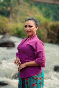 Asian woman standing in front of the river while wearing a purple dress with beautiful makeup and river in the background inside the village