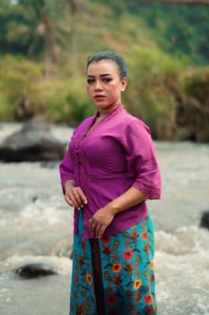 Asian woman standing in front of the river while wearing a purple dress with beautiful makeup and river in the background inside the village