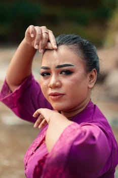 A close-up shot of a beautiful Asian woman with makeup while wearing a traditional purple dress called kebaya near the river