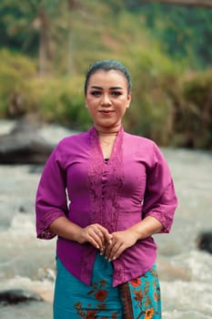 Asian woman standing in front of the river while wearing a purple dress with beautiful makeup and river in the background inside the village