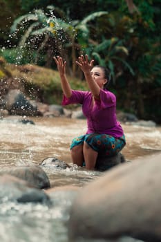 Asian woman playing with dirty water from a dirty river while wearing a purple dress and green skirt near the river