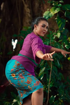 Sexy Sundanese woman with purple dress dancing in front of the big tree and the green leaves in the background during the daylight