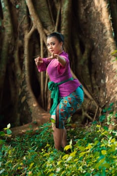 Sexy Asian woman dancing pose while wearing a beautiful purple dress and green belt on her body in front of the big brown tree inside the forest