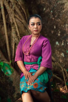 An Asian woman beautifully sitting on the big tree in a purple dress while visiting the jungle in the daylight