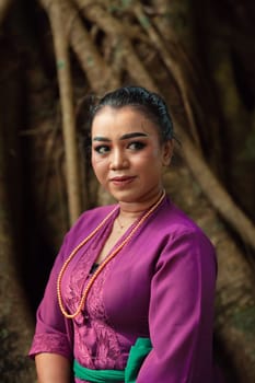 An Asian woman beautifully sitting on the big tree in a purple dress while visiting the jungle in the daylight