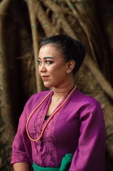 An Asian woman beautifully sitting on the big tree in a purple dress while visiting the jungle in the daylight