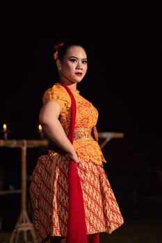 Brave Balinese woman poses with an angry expression while wearing a traditional orange dress and makeup during the dance festival