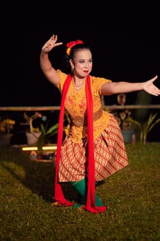 Balinese dancer with an orange costume and wearing makeup posing like a dancer while in black hair inside the village
