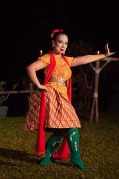 Balinese dancer with an orange costume and wearing makeup posing like a dancer while in black hair inside the village