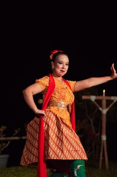 Balinese dancer with an orange costume and wearing makeup posing like a dancer while in black hair inside the village