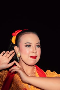 Exotic Javanese woman wearing beautiful makeup with red lips while wearing a traditional yellow costume and red scarf inside the village