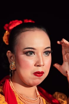 Exotic Javanese woman wearing beautiful makeup with red lips while wearing a traditional yellow costume and red scarf inside the village