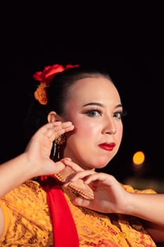 Exotic Javanese woman wearing beautiful makeup with red lips while wearing a traditional yellow costume and red scarf inside the village