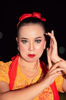 Exotic Javanese woman wearing beautiful makeup with red lips while wearing a traditional yellow costume and red scarf inside the village