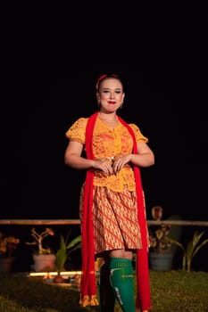 Indonesian woman with a gorgeous orange batik dress wearing a red scarf and red lips on her face standing inside the stage