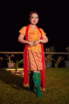 Indonesian woman with a gorgeous orange batik dress wearing a red scarf and red lips on her face standing inside the stage