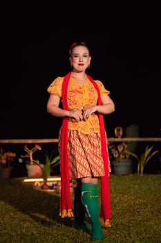Indonesian woman with a gorgeous orange batik dress wearing a red scarf and red lips on her face standing inside the stage