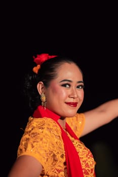 Close-up face of a Balinese woman during the traditional dance performance while wearing an orange costume and makeup on the stage
