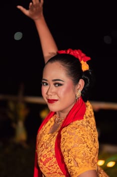 Close-up face of a Balinese woman during the traditional dance performance while wearing an orange costume and makeup on the stage
