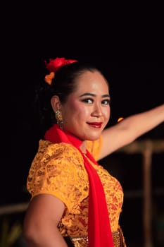 Close-up face of a Balinese woman during the traditional dance performance while wearing an orange costume and makeup on the stage