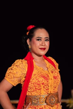 Exotic Indonesian women with red lips and makeup while wearing an orange dress and red scarf during the traditional dance festival