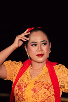 Exotic Indonesian women with red lips and makeup while wearing an orange dress and red scarf during the traditional dance festival